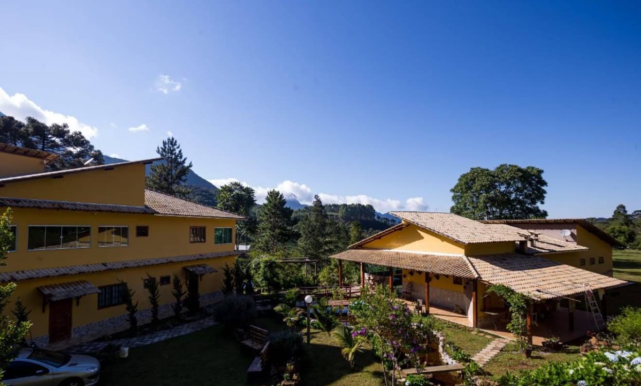 Jardim da pousada com araucárias e montanhas da região do Pico da Bandeira ao fundo