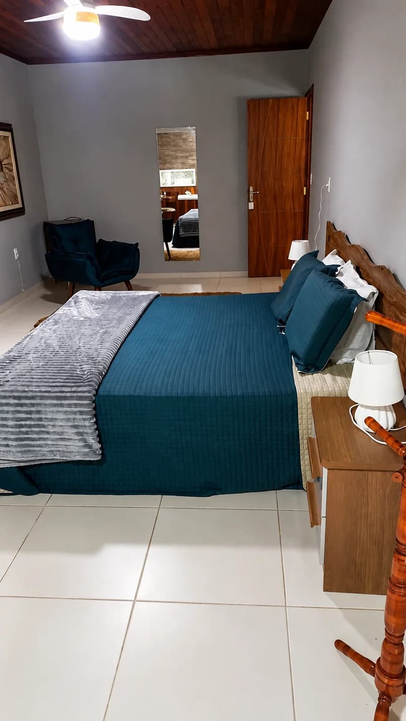 Vista do quarto da Suíte Araucária, com a cama e a poltrona junto à janela