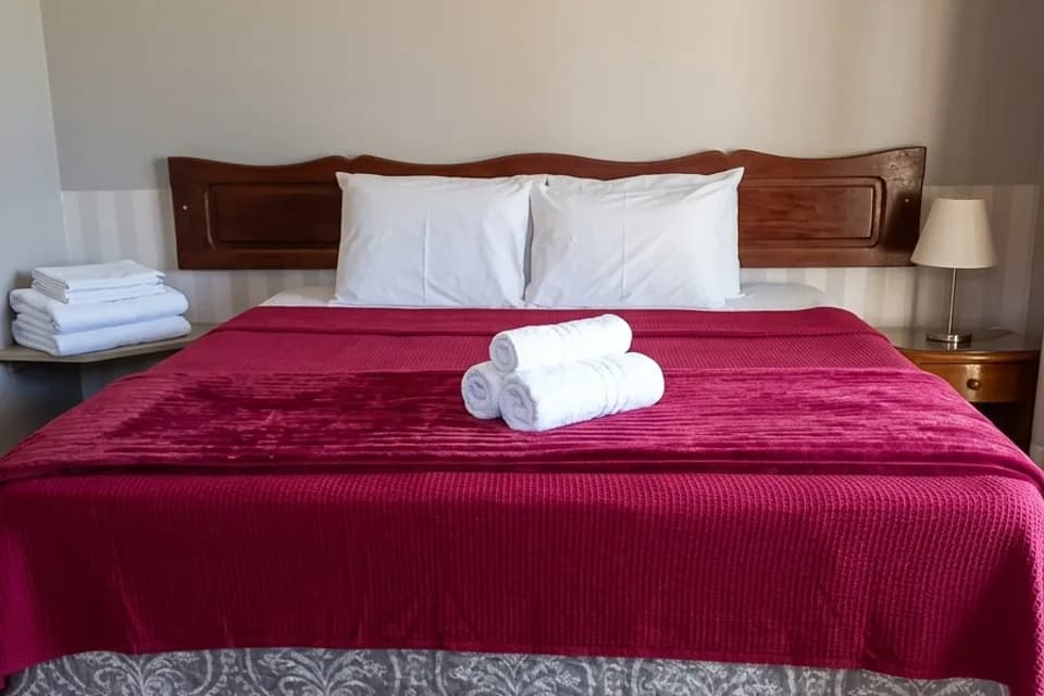 Cama de casal da Suíte Colinas, com colcha vinho e cabeceira de madeira