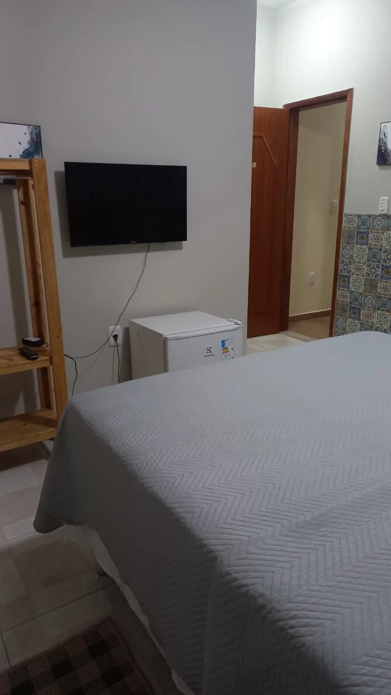 TV na parede do quarto da Suíte Manacá, com frigobar ao lado