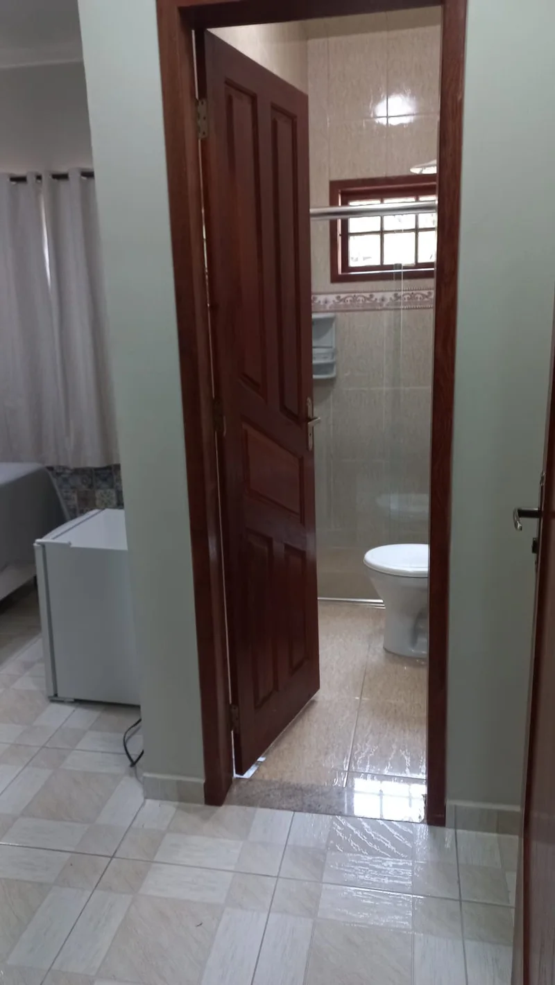 Entrada do banheiro da Suíte Manacá, com porta de madeira e vaso sanitário ao fundo