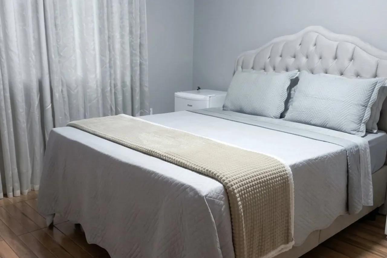 Cama de casal da Suíte Vale, com cabeceira capitonê e piso de madeira
